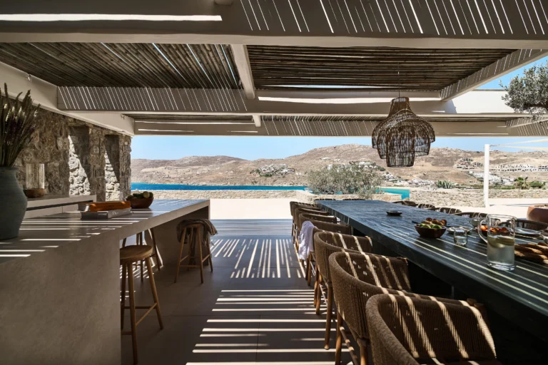 Long dining table on a shaded terrace with a sea view at a villa in Mykonos